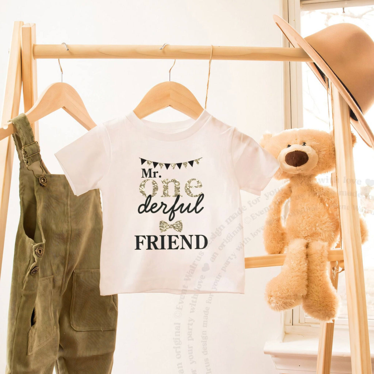 White Mr Onederful Friend toddler tee on a wooden clothes rack beside a teddy bear.