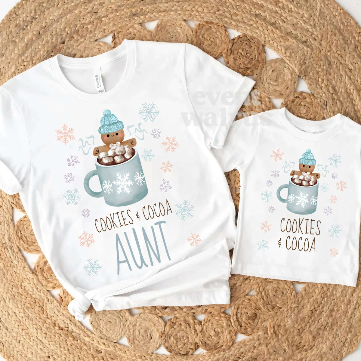 White Aunt Cookies and Cocoa tee and a matching kids tee on a round jute rug.