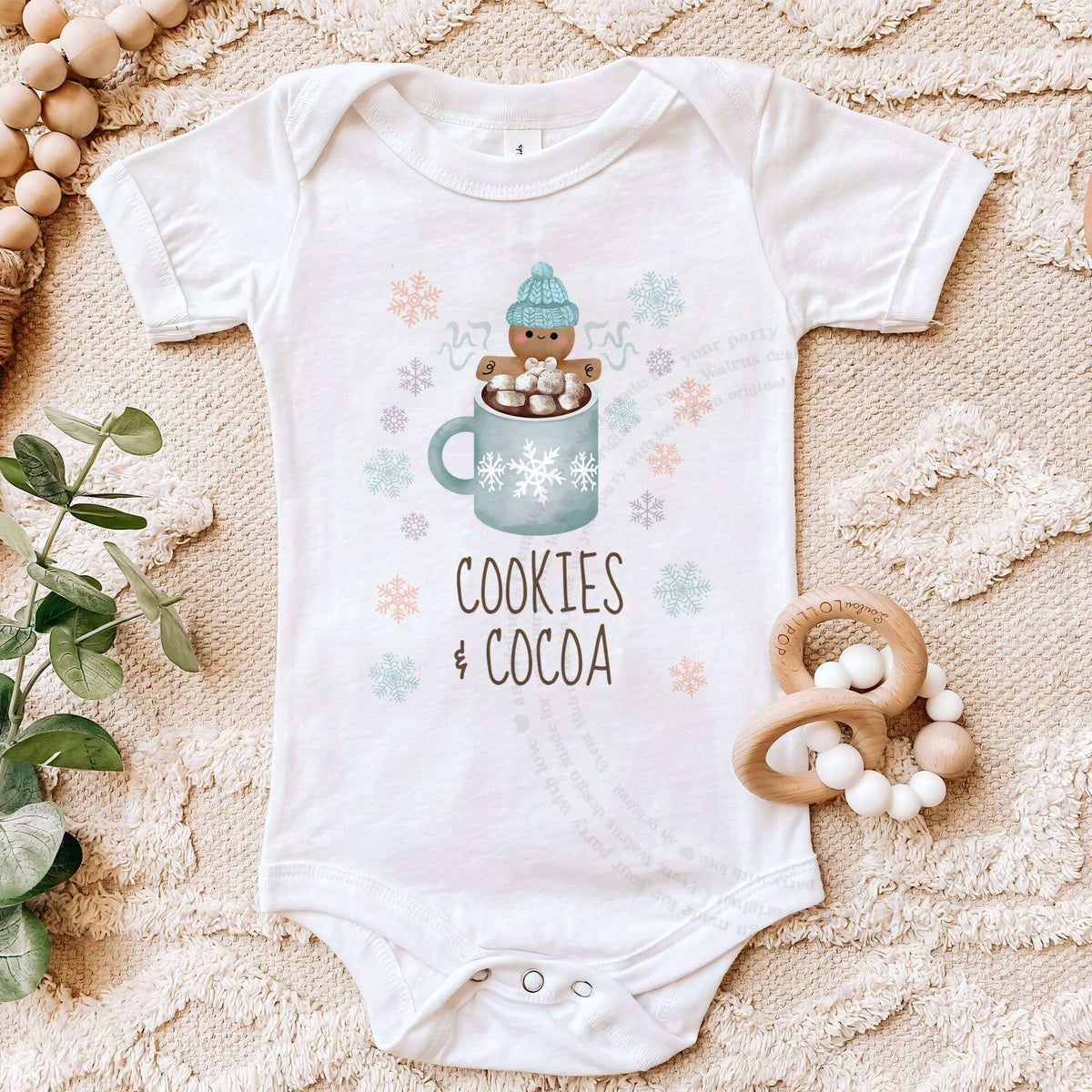 White Cookies and Cocoa bodysuit on a beige blanket with a wooden teether.