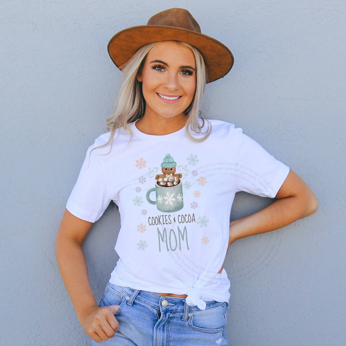 Smiling woman in a brown felt hat wearing a Cookies and Cocoa Mom shirt with a blue mug.