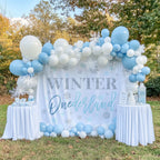 Winter onederland boy backdrop on a lawn with a blue balloon garland and two white dessert tables.