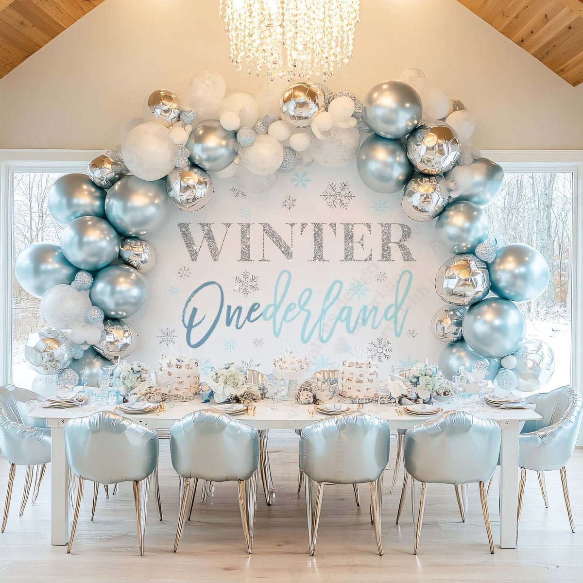 Blue winter onederland backdrop behind a party table with silver and blue balloons and a chandelier.