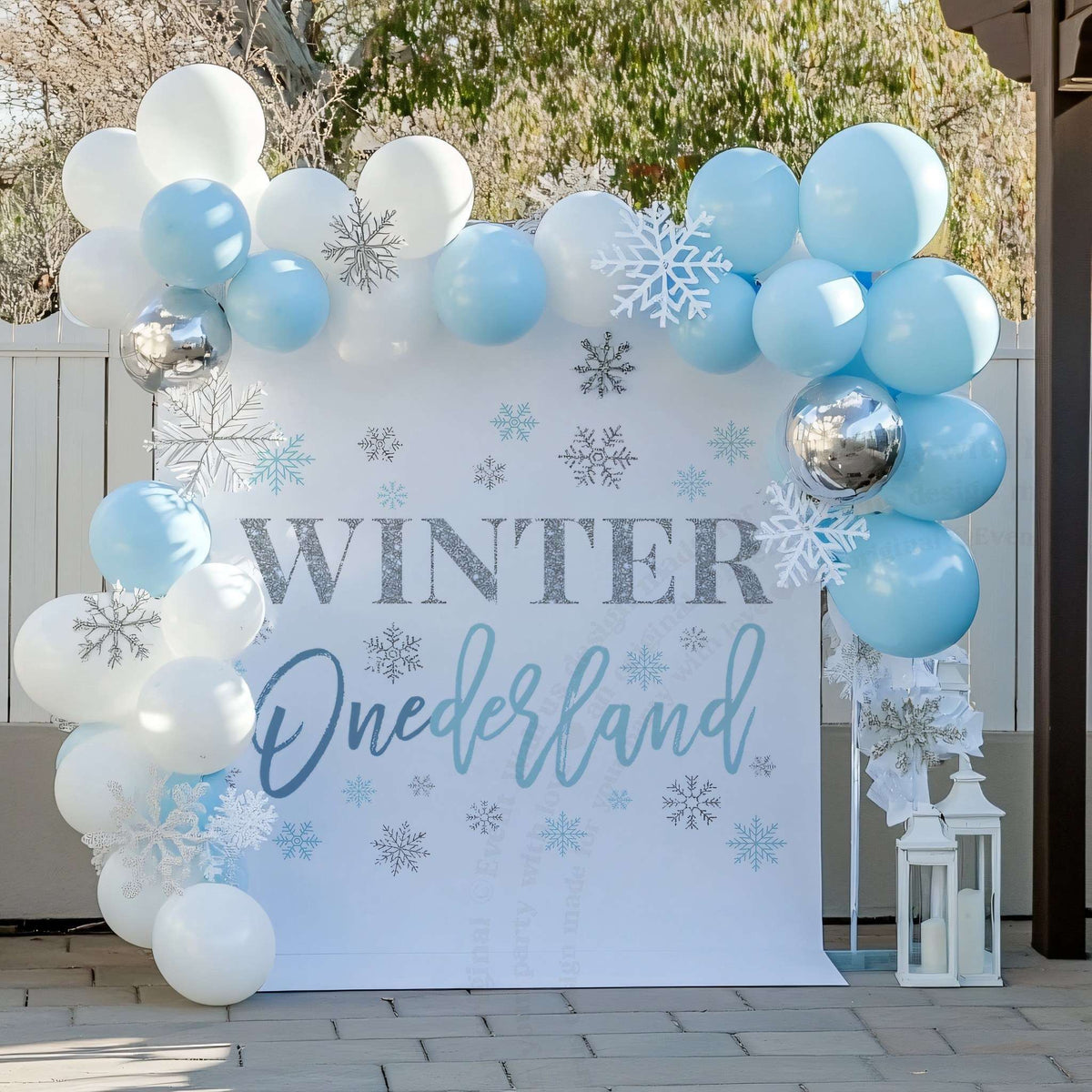 Blue winter onederland first birthday backdrop on a porch with pale blue balloons and a white lantern.