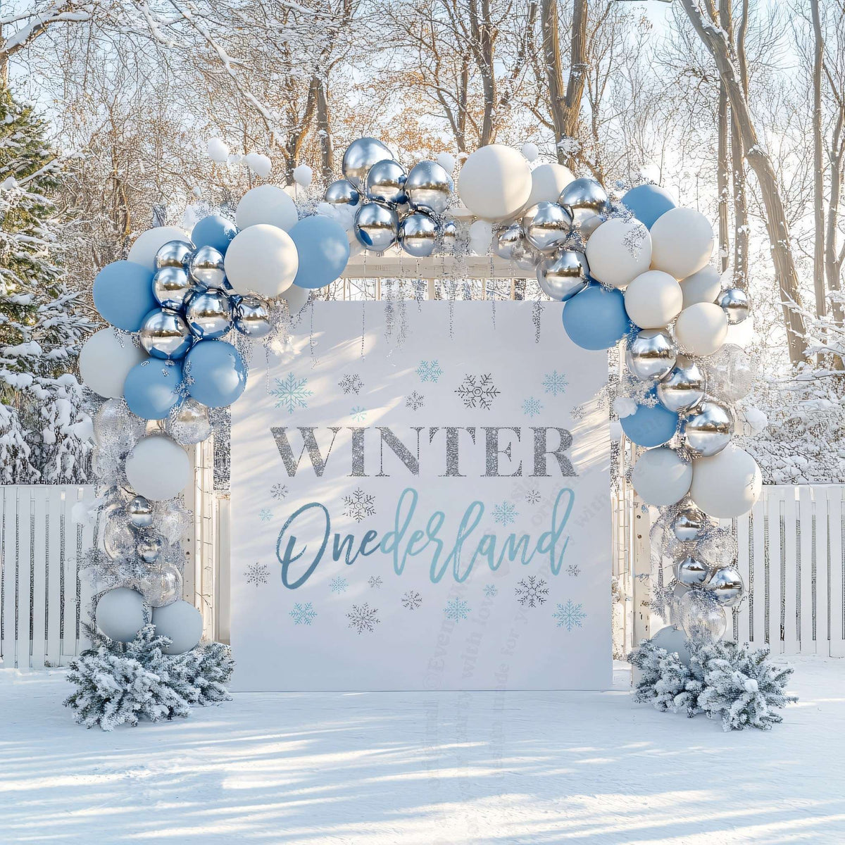 Blue glitter winter onederland backdrop in a snowy garden under a blue, white and silver balloon arch.
