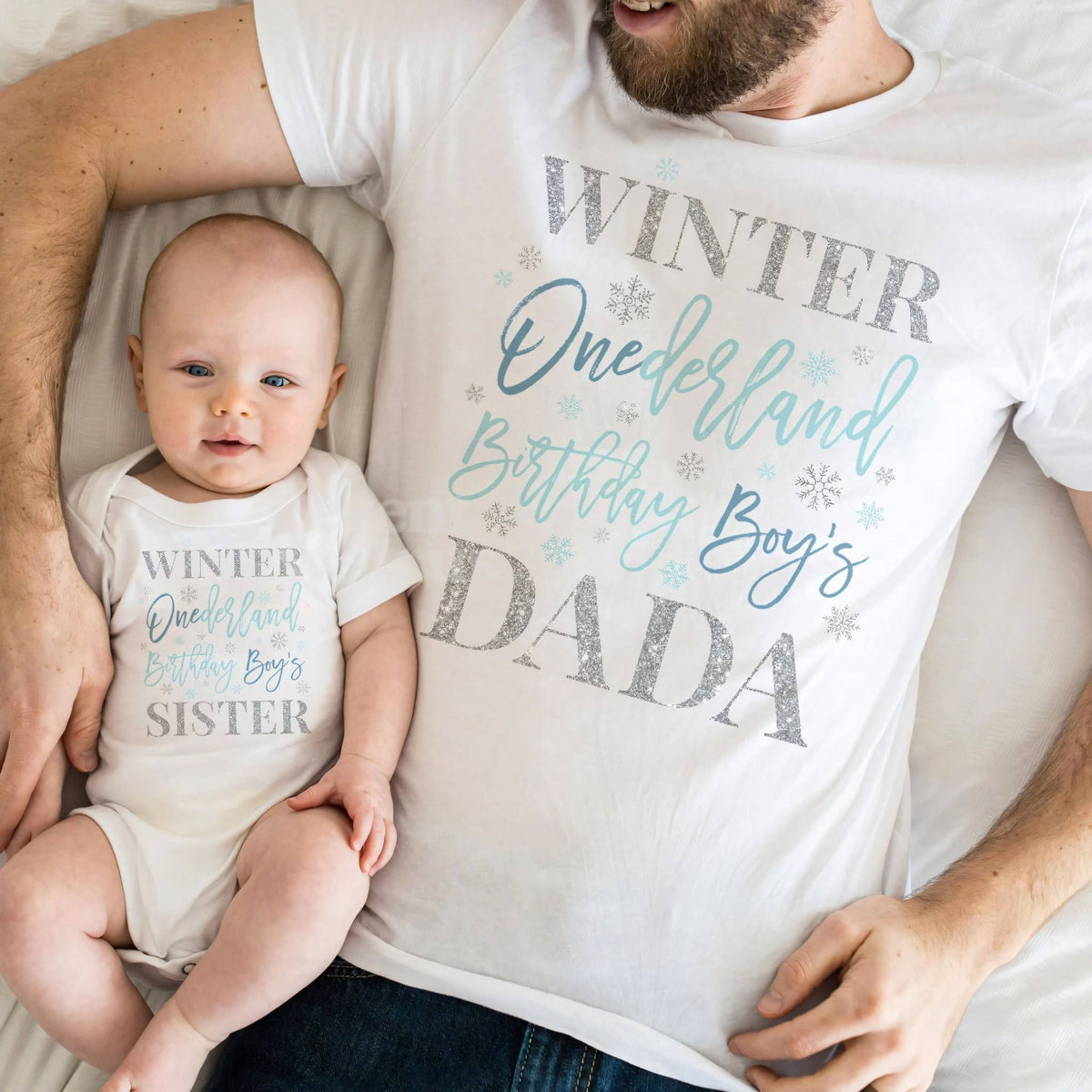 Baby in a white Winter Onederland Sister bodysuit lying on Dad in his Dada shirt.