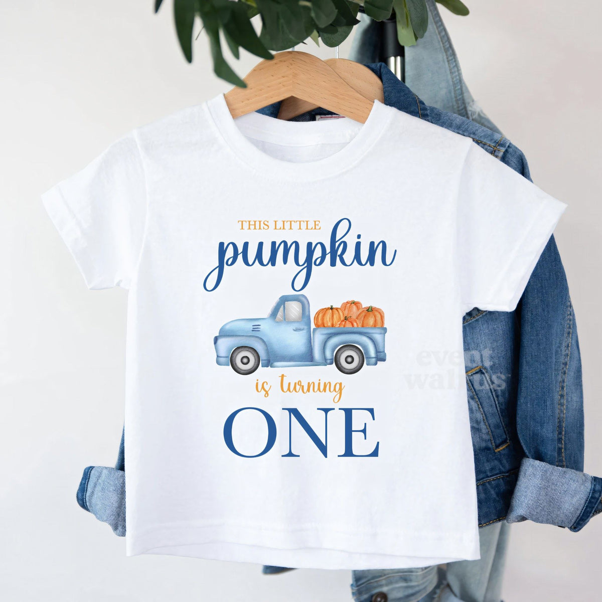 White This Little Pumpkin Is Turning One toddler tee on a hanger over a denim jacket.