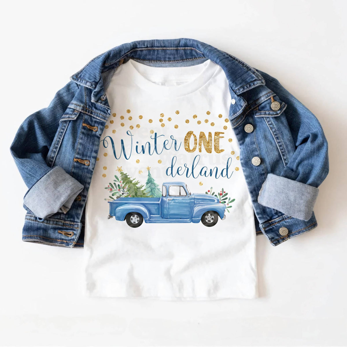 White blue truck Winter ONE derland toddler tee laid on a denim jacket.