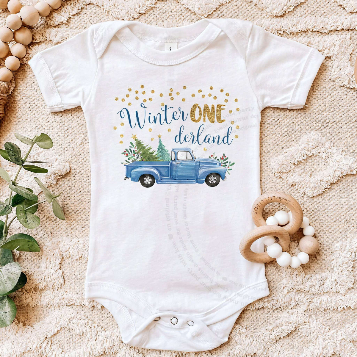 White blue truck bodysuit on a beige blanket with a wooden teether.