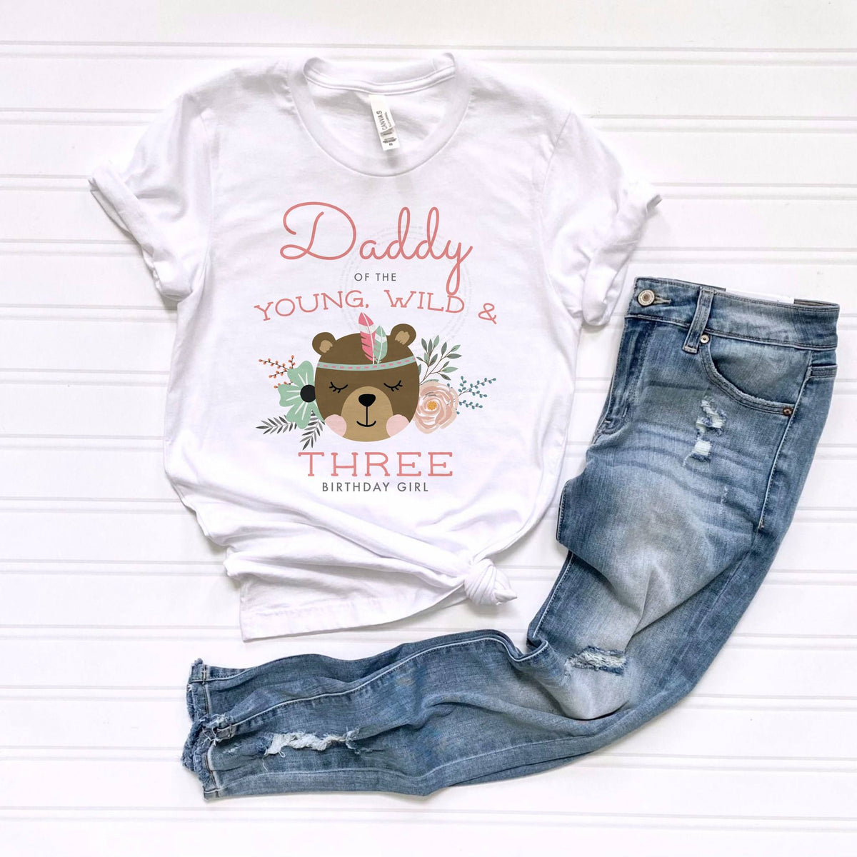 White Daddy of the Young, Wild and Three tee laid flat beside jeans.