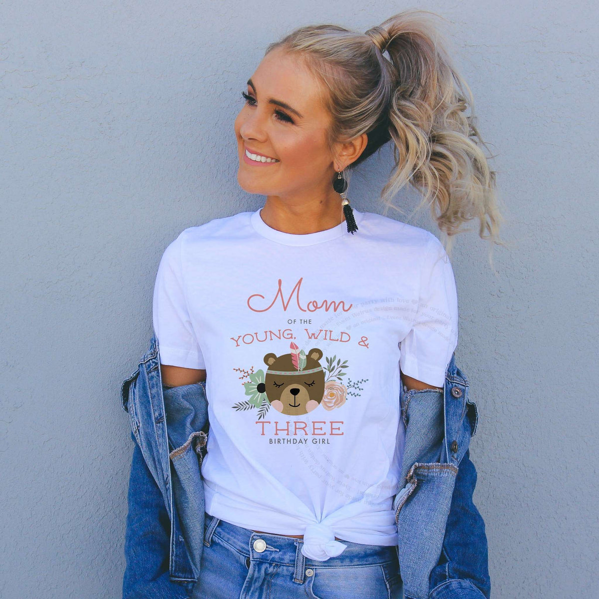 Woman in a denim jacket wearing a Mom of the Young, Wild and Three shirt with a floral bear.