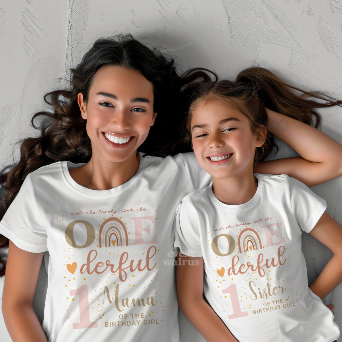 Mom and big sister lying together in white Mama and Sister boho rainbow Onederful shirts.