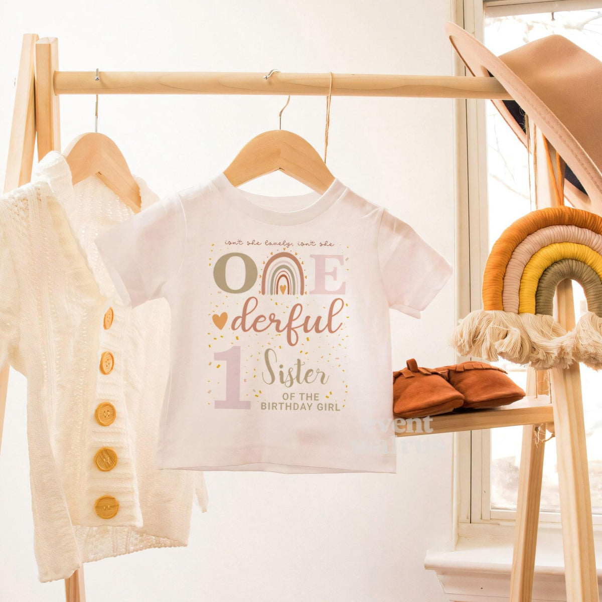 White toddler Sister of the Birthday Girl tee on a hanger beside a boho rainbow.