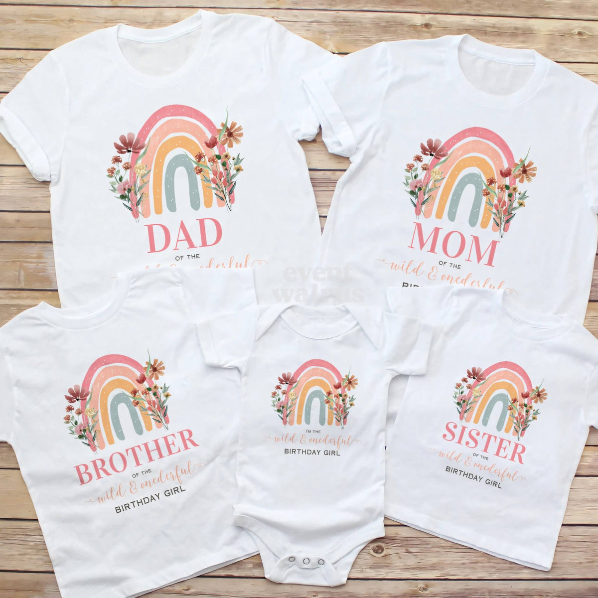 Dad, Mom, Brother, Sister and baby rainbow Wild and Onederful shirts laid out on wood.