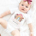 Baby girl with a pink bow lying in a white Wild and Onederful Birthday Girl bodysuit.