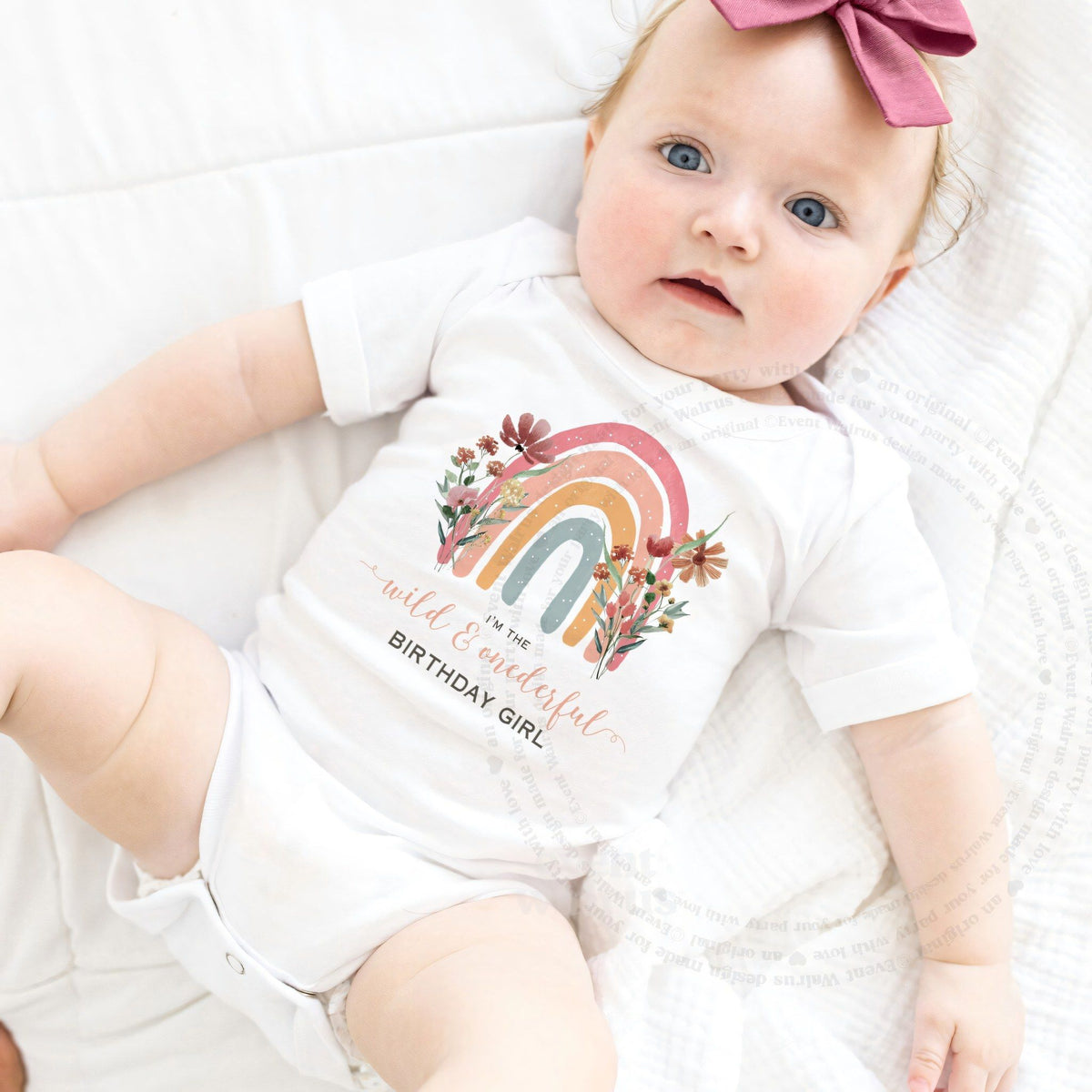 Baby girl with a pink bow lying in a white Wild and Onederful Birthday Girl bodysuit.