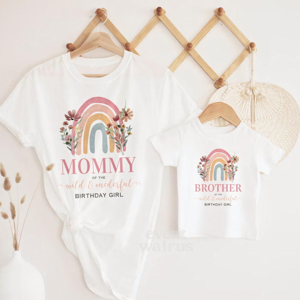 White Mommy and Brother rainbow Wild and Onederful tees hanging on a wooden peg rail.