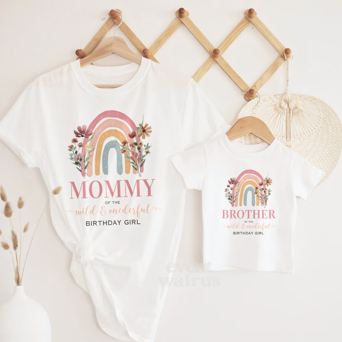 White Mommy and Brother rainbow Wild and Onederful tees hanging on a wooden peg rail.