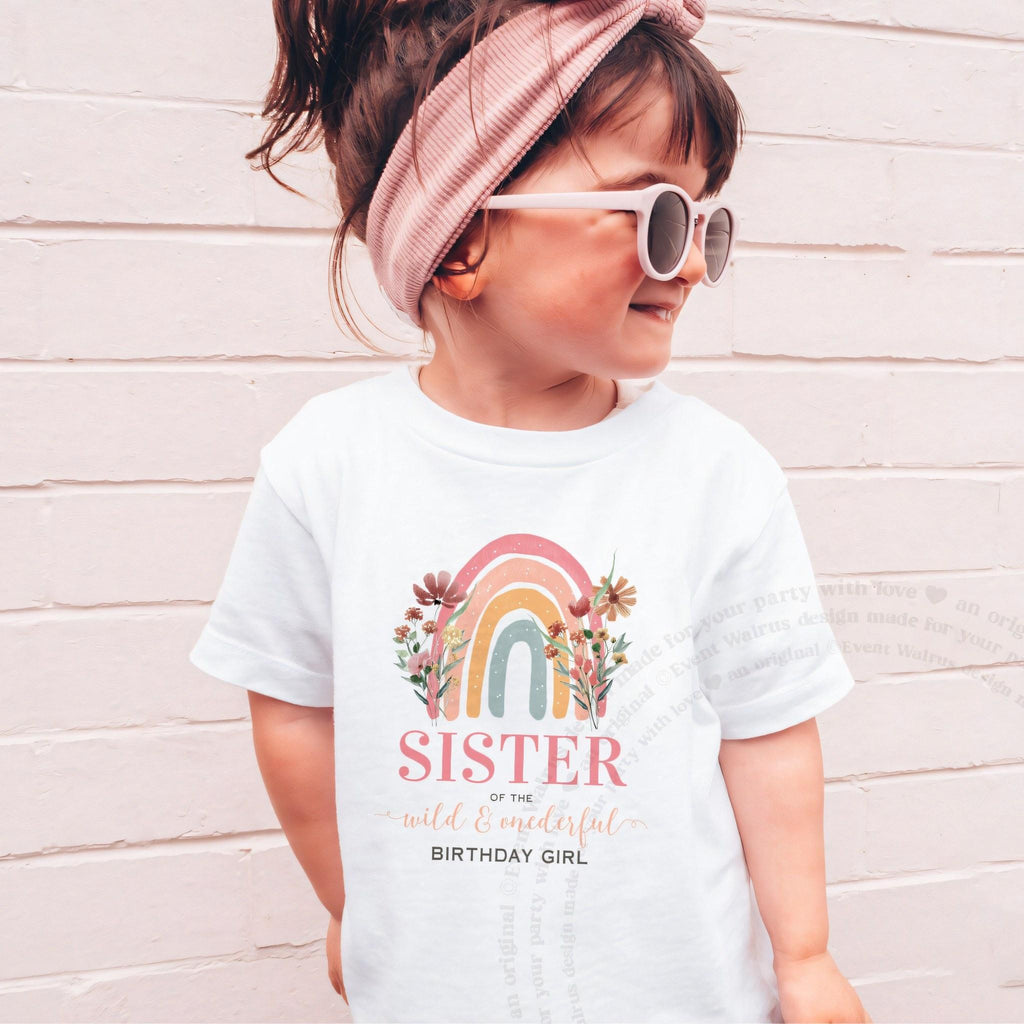 Girl in sunglasses and a pink headband wearing a white rainbow Sister of the Wild and Onederful shirt.