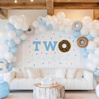 Chocolate donut backdrop behind a white sofa and a sprinkle cake on a wood table.