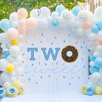 Two sweet chocolate donut backdrop in a garden with white, peach and yellow balloons.