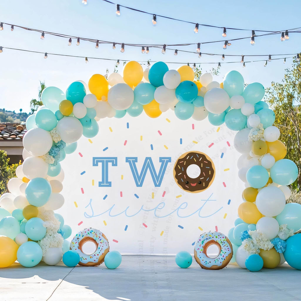 Two sweet donut backdrop on a patio with teal, yellow and white balloons.