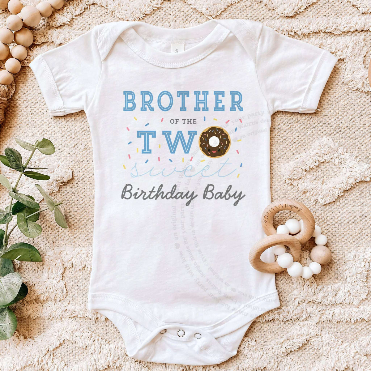 White Brother of the Two Sweet bodysuit on a beige blanket with a wooden teether.
