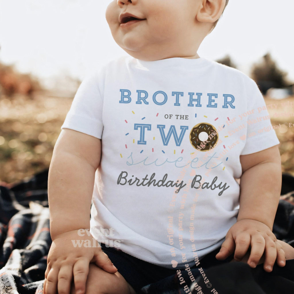 Baby sitting outdoors on a blanket in a white Brother of the Two Sweet baby tee.