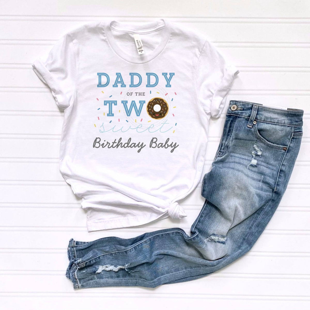 White Daddy of the Two Sweet tee laid flat beside jeans.
