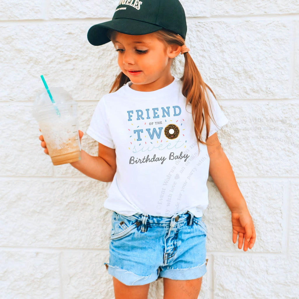 Girl in a ball cap holding a drink in a white Friend of the Two Sweet shirt.
