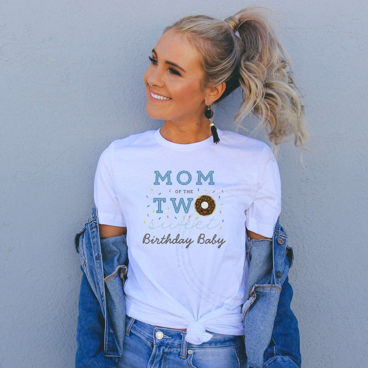 Woman in a denim jacket wearing a Mom of the Two Sweet shirt with a chocolate donut.