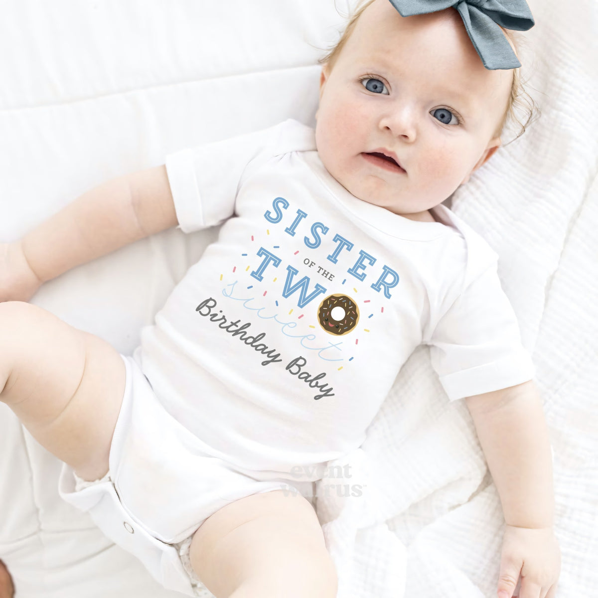 Baby girl with a blue bow lying in a white Sister of the Two Sweet bodysuit.
