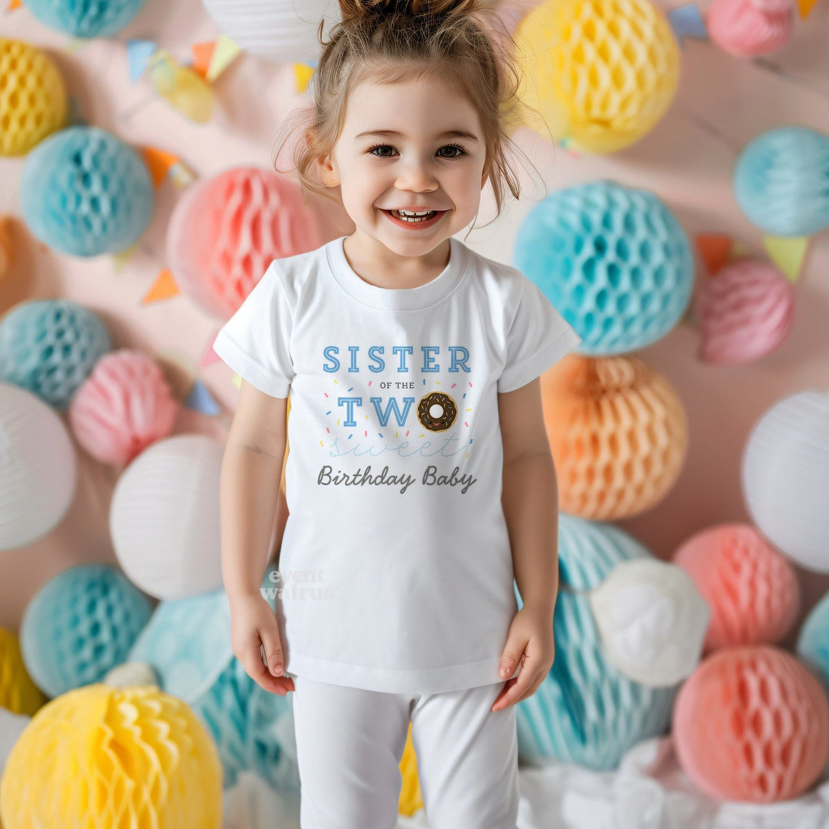 Smiling toddler girl among paper honeycomb balls in a white Sister of the Two Sweet tee.