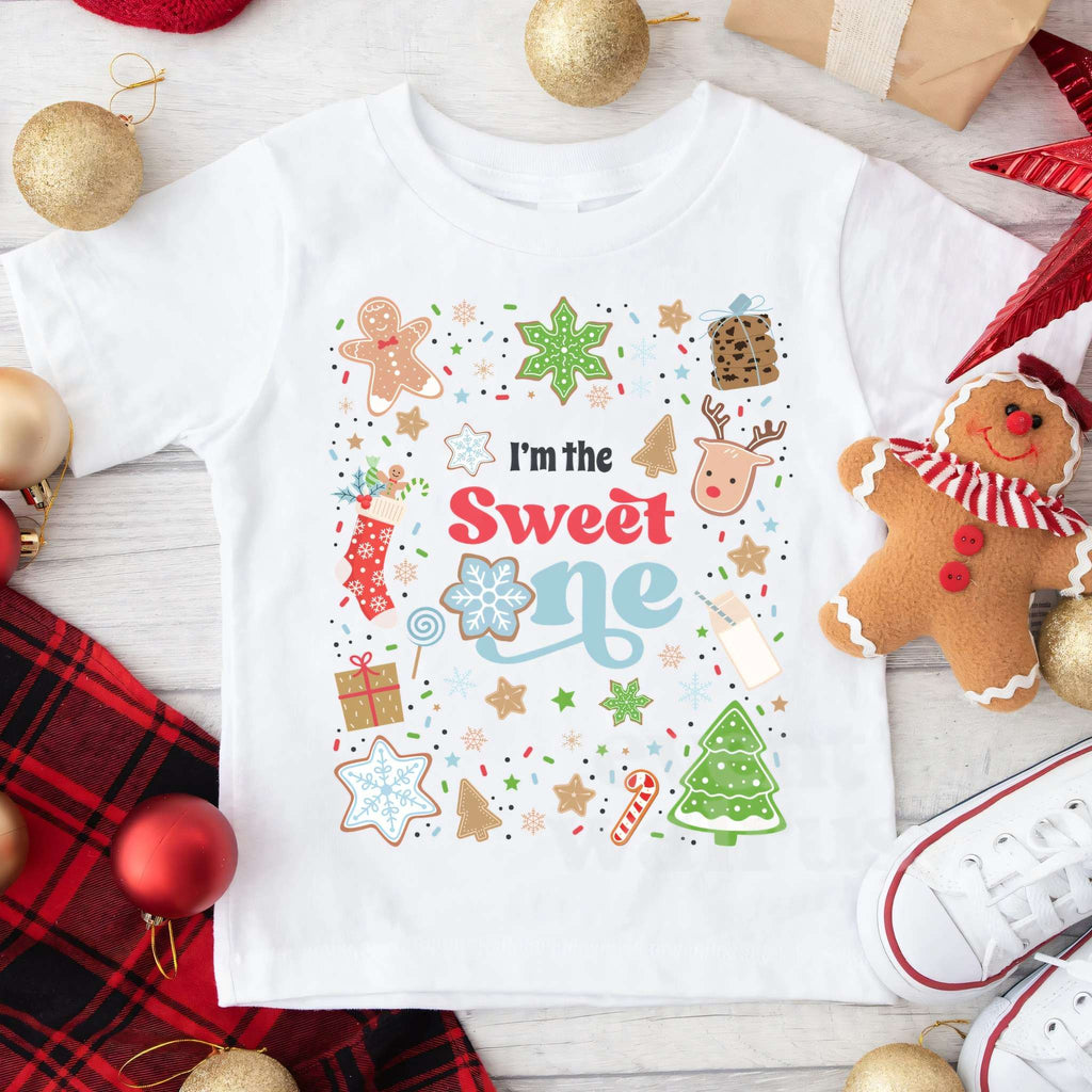 White I'm the Sweet One tee laid flat with ornaments, a gingerbread man and red plaid.
