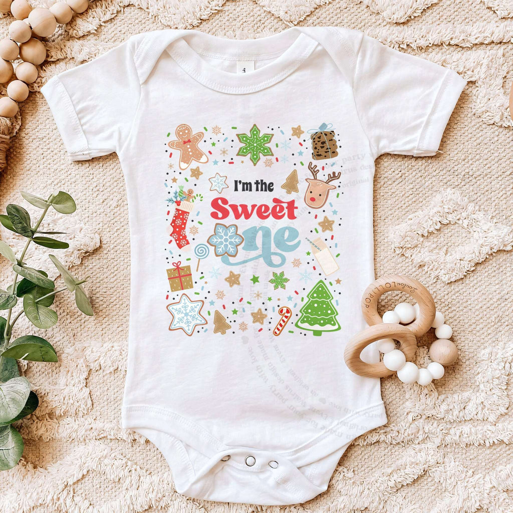 White I'm the Sweet One bodysuit on a beige blanket with a wooden teether.