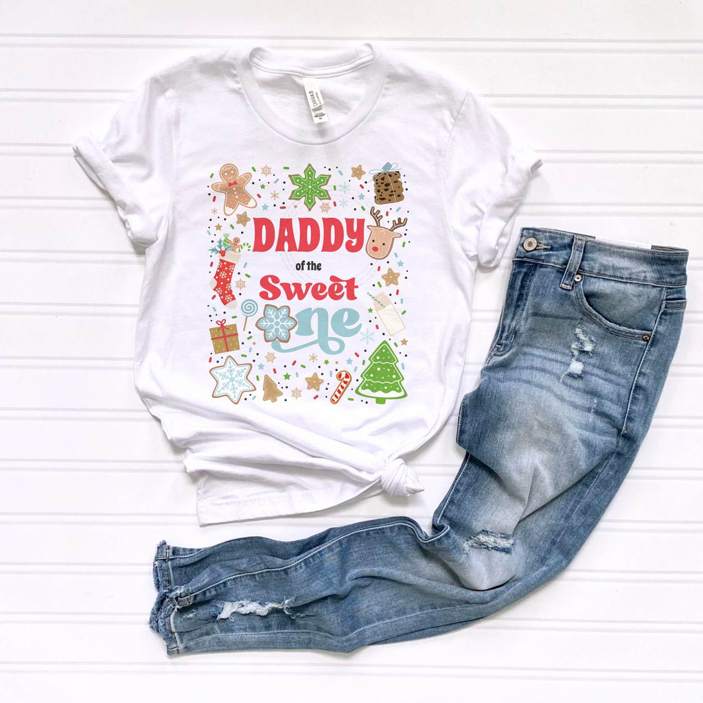 White Daddy of the Sweet One tee with gingerbread, candy canes and snowflakes, laid flat beside jeans.