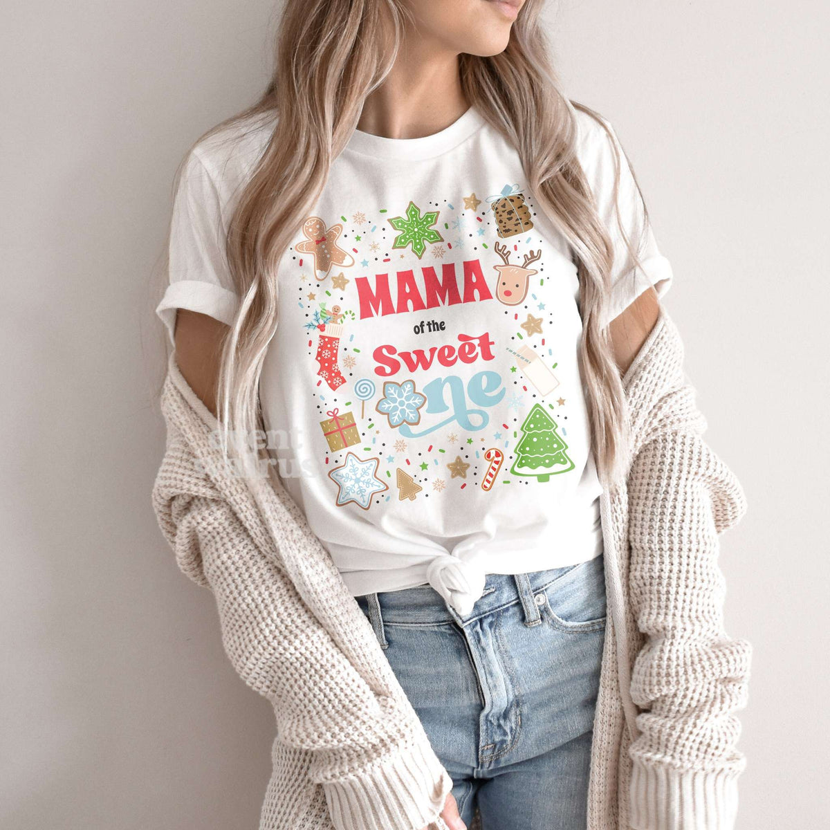 Woman in a knit cardigan wearing a white Mama of the Sweet One shirt.