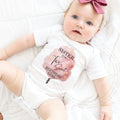 Baby girl with a pink bow lying in a white Sister of the Two Sweet bodysuit.