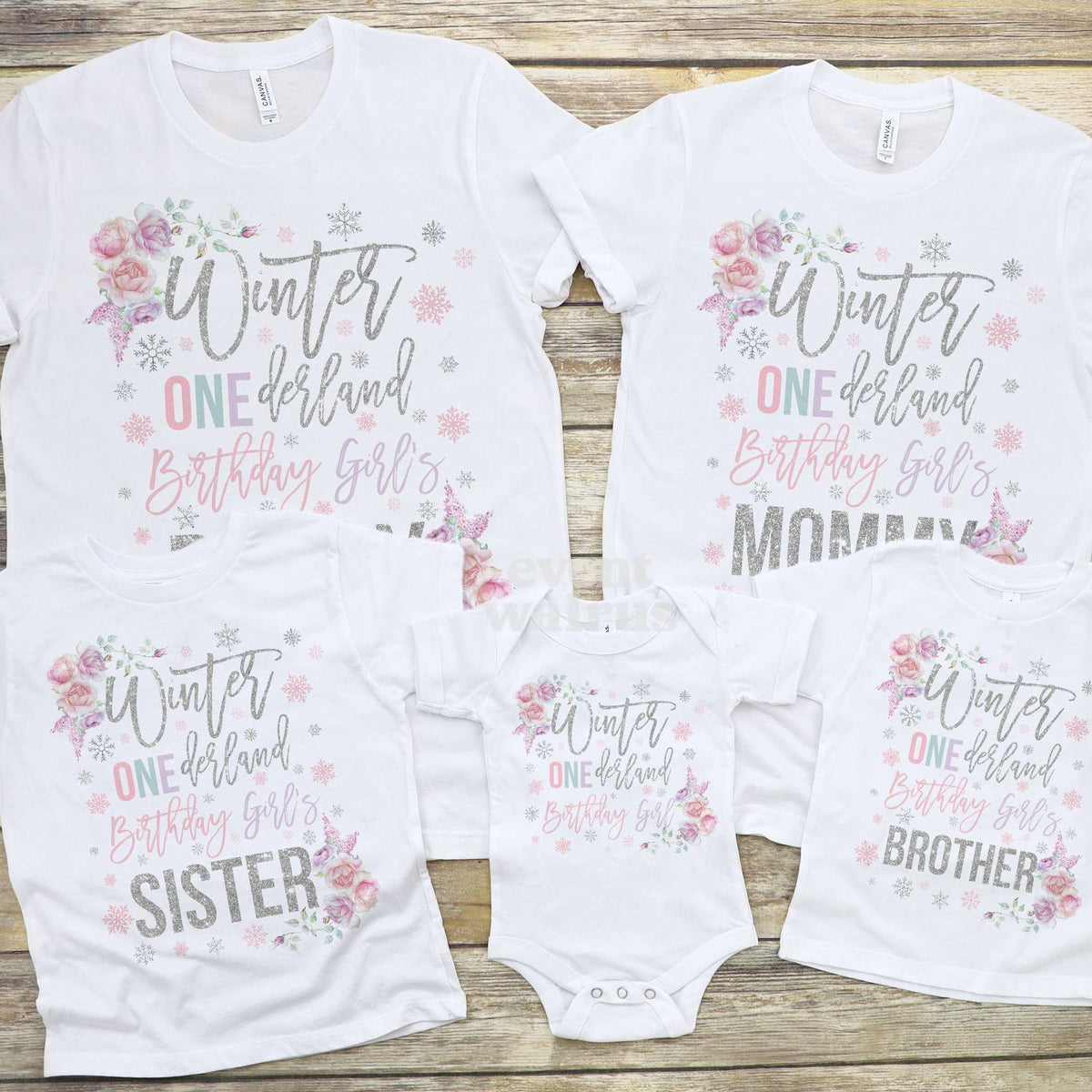 Floral Winter ONEderland bodysuit laid out with the family's shirts on wood.