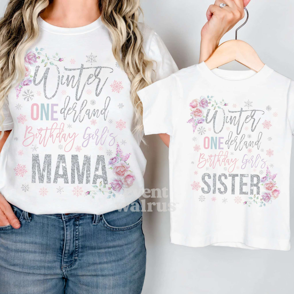 Mom holding up a white Sister floral Winter ONEderland tee on a hanger while wearing her Mama shirt.