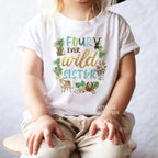 Girl in a black hat sitting on a stool in a white Four Ever Wild Sister tee.