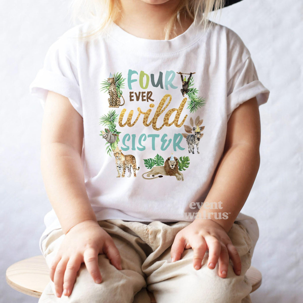 Girl in a black hat sitting on a stool in a white Four Ever Wild Sister tee.