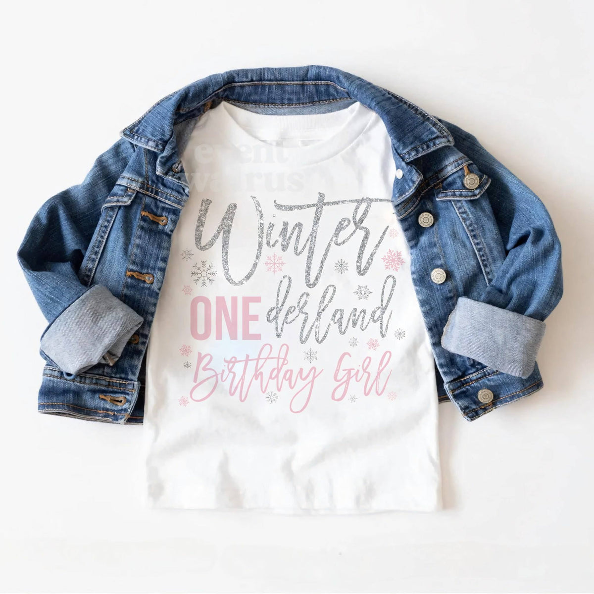 White Winter ONEderland Birthday Girl toddler tee laid on a denim jacket.