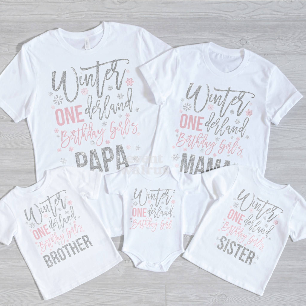 Papa, Mama, Brother, Sister and baby Winter ONEderland shirts laid out on gray wood.