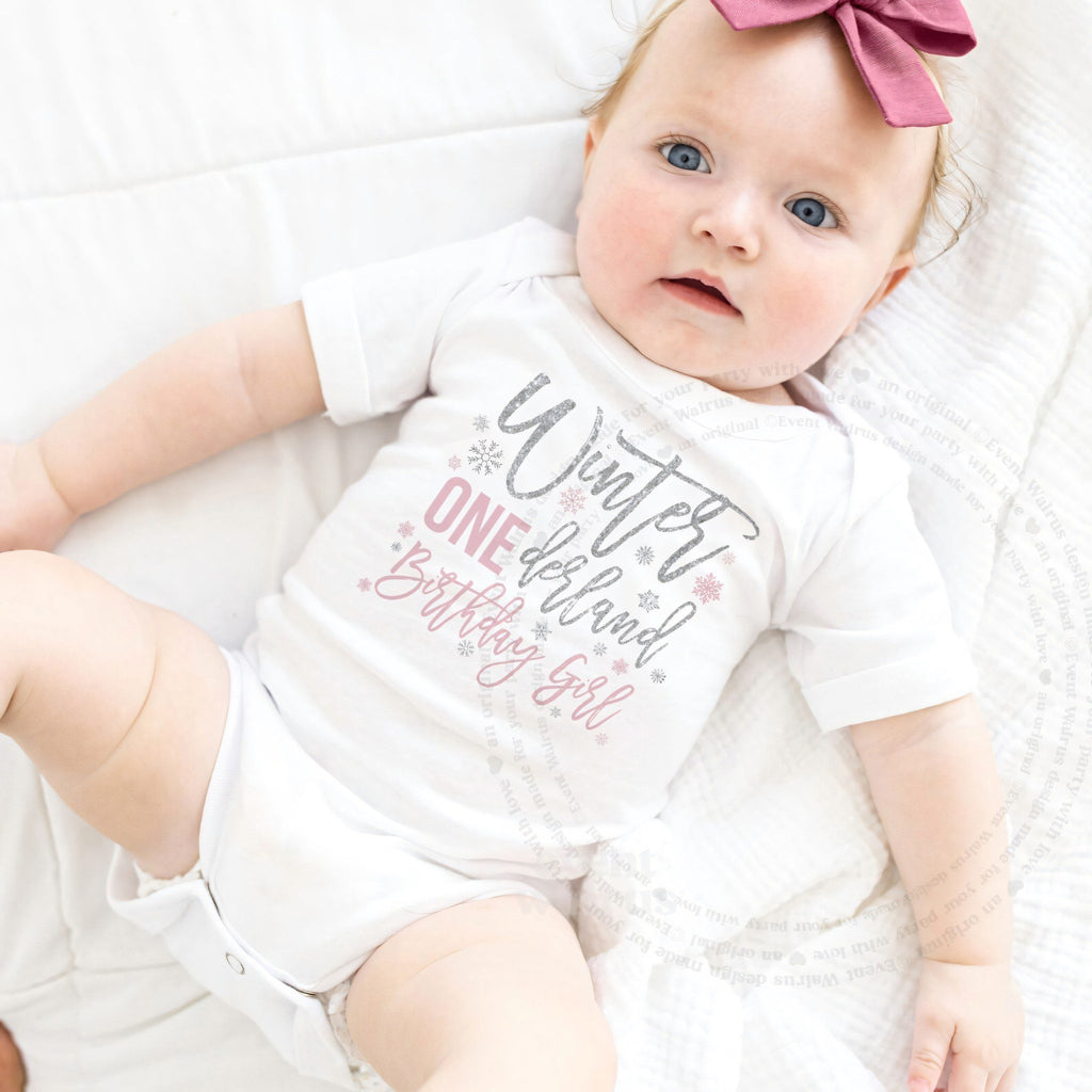 Baby girl with a pink bow lying in a white Winter ONEderland Birthday Girl bodysuit.