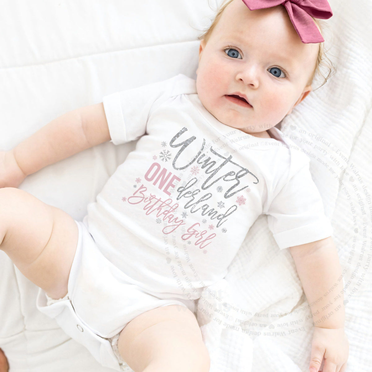 Baby girl with a pink bow lying in a white Winter ONEderland Birthday Girl bodysuit.