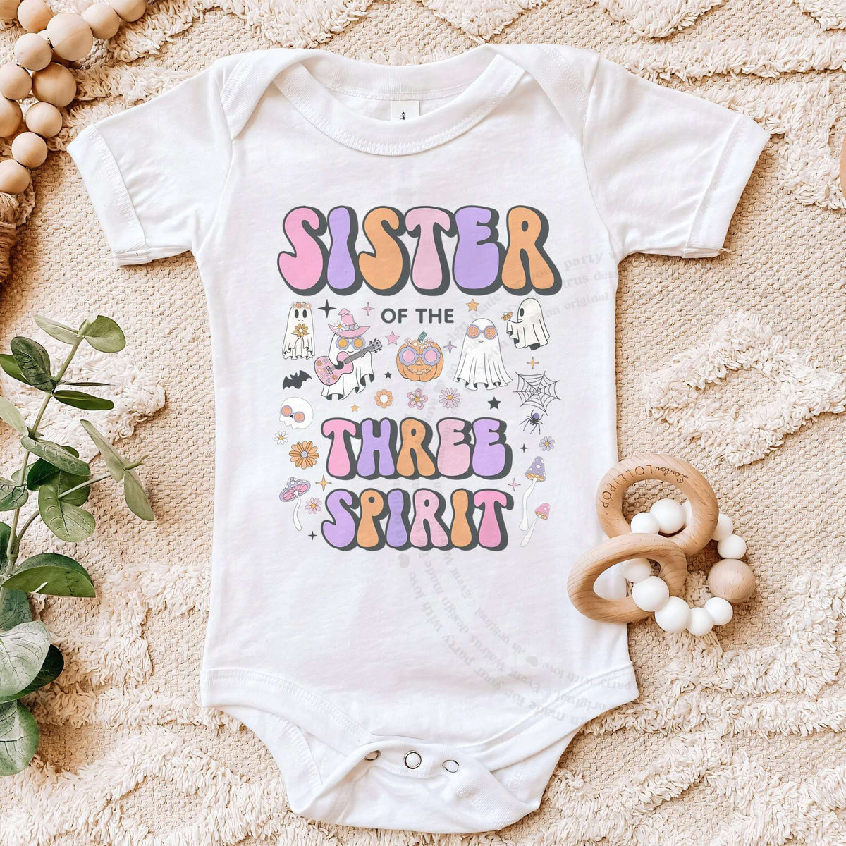 White Sister of the Three Spirit bodysuit on a beige blanket with a wooden teether.