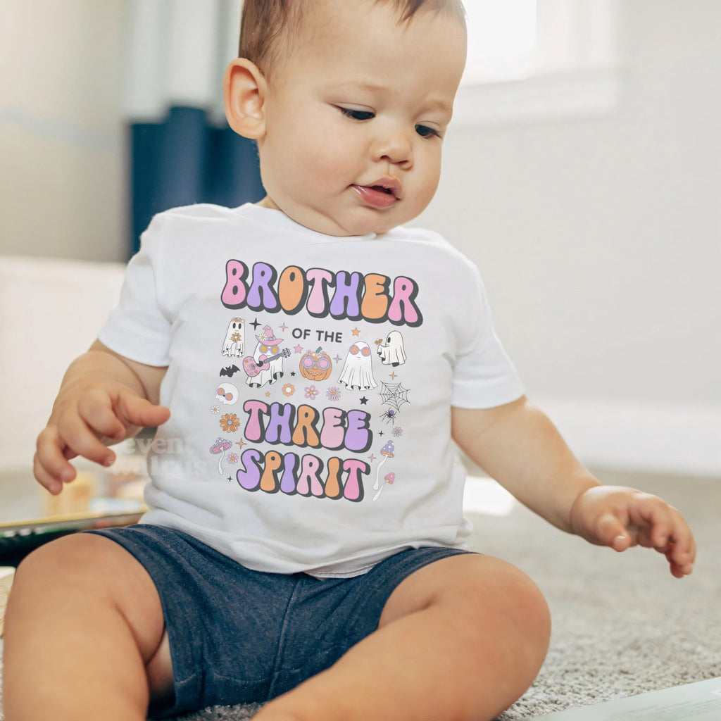 Baby boy sitting on a rug in a white Brother of the Three Spirit baby tee.