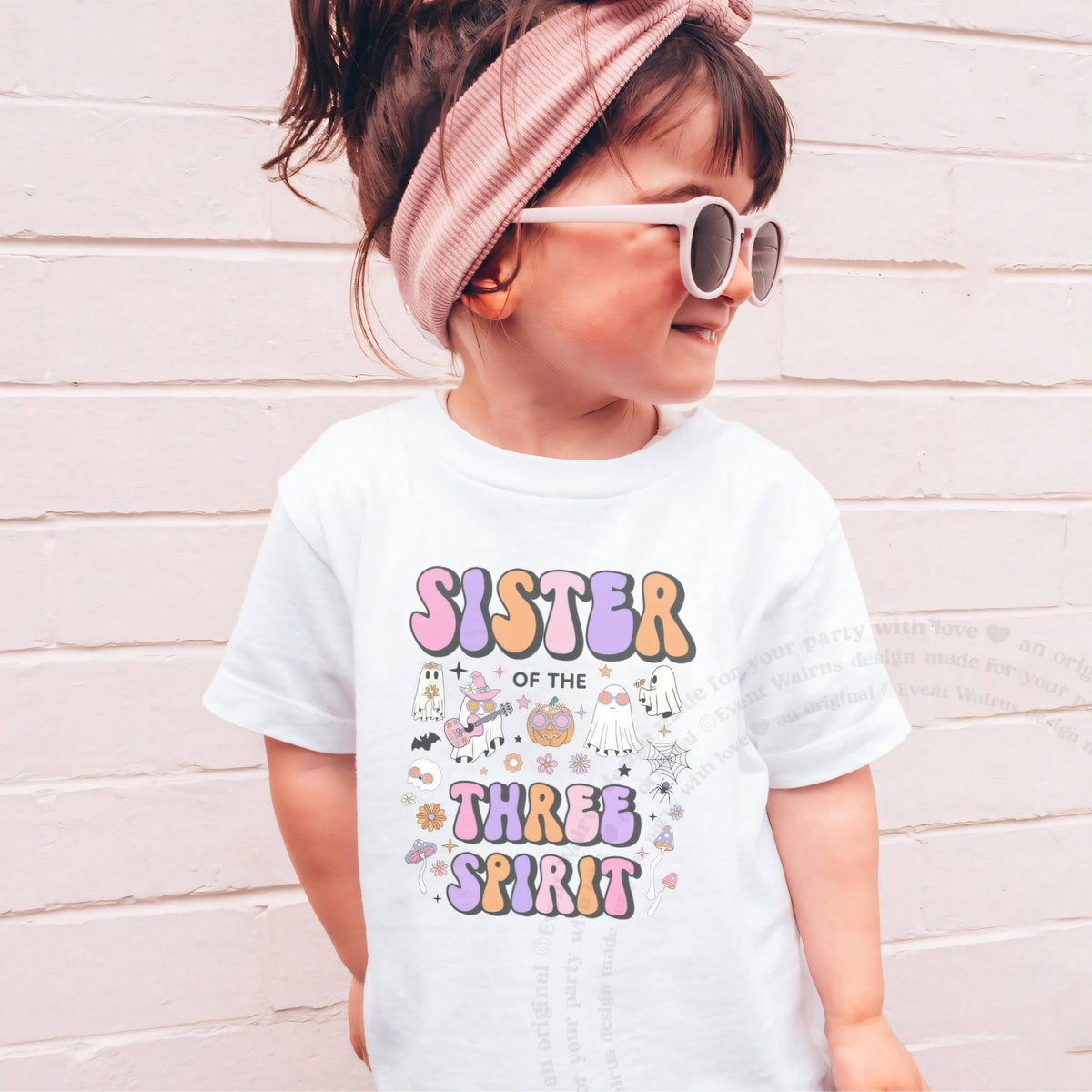 Girl in sunglasses and a pink headband wearing a white Sister of the Three Spirit shirt.