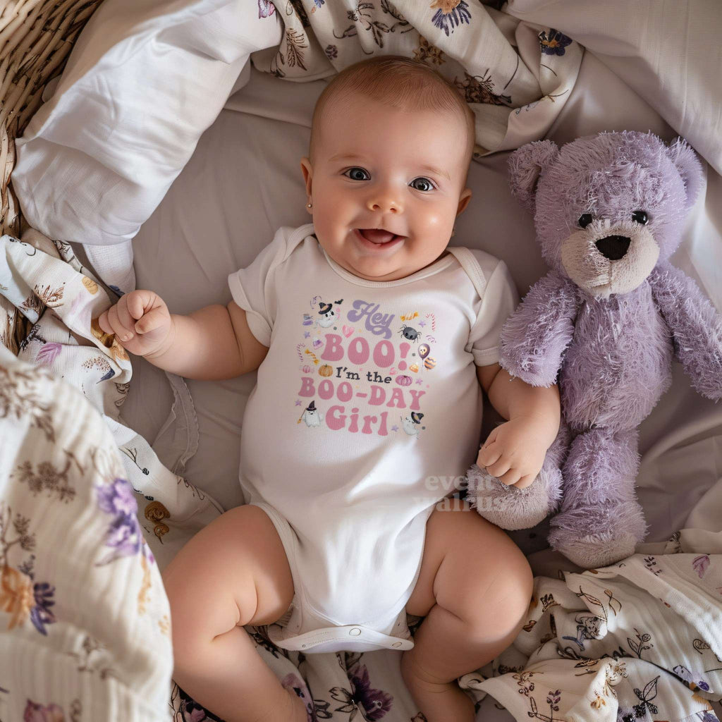 Smiling baby beside a purple teddy bear in a white Hey Boo Boo-Day Girl bodysuit.