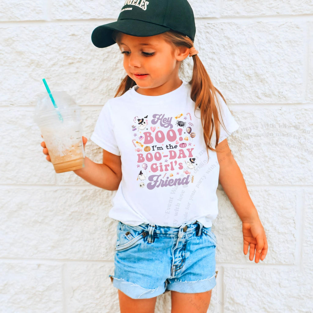 Girl in a ball cap holding a drink in a white Hey Boo Friend shirt.